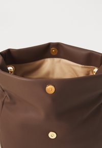 Braune Ledertasche mit goldenen magnetischen Druckknöpfen und beigem Stofffutter, von oben geöffnet gezeigt.