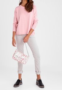 Różowy sweter z długim rękawem, jasnoszare spodnie z mankietami, torebka w kwiatowy wzór z łańcuszkiem oraz czarne buty na sznurówki.