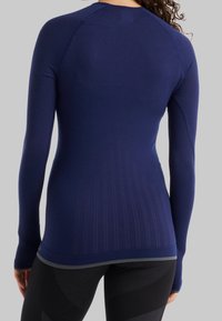 Námořnický dlouhý rukáv atletického topu vyrobený z texturované tkaniny. Disponuje těsným střihem, raglánovými rukávy a vertikálními pruhy na zádech.