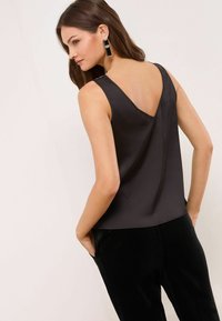 Melnas satīna bezpiedurkņu blūze ar V formas aizmuguri, ar gludu tekstūru. Kombinēta ar melniem samta biksēm. Vienkārša un eleganta siluets.