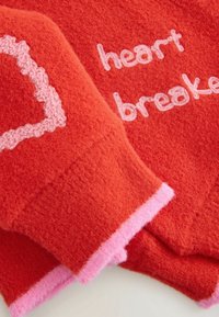 Tissu rouge duveteux avec texte rose "heart breaker" et forme de cœur brisé rose cousue aux bords des poignets de manche.