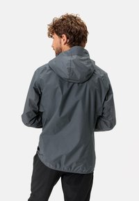 Giacca a vento da uomo in grigio scuro, realizzata in tessuto leggero e idrorepellente. Presenta polsini elasticizzati e un orlo posteriore più lungo per una maggiore copertura.