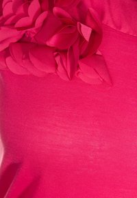 Helderroze stof met getextureerde bloemaccenten en glad, rekbaar materiaal. Het ontwerp bevat gelaagde bloemblaadjes-achtige details.