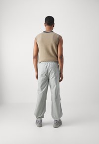 Beige sleeveless knit top with a crew neck, paired with loose, light gray cargo pants. Smooth texture, elastic waist, and side pockets visible.