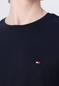 Camiseta de algodón azul marino con cuello redondo, que presenta un pequeño logo bordado en rojo, blanco y azul en el pecho.