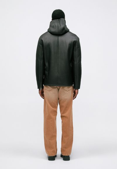 Schwarze Lederjacke mit Kapuze, glatte Textur, taillierter Schnitt; kombiniert mit weiten, hellbeigen Hosen. Die Rückansicht zeigt keine weiteren Details.