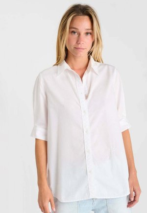 Weißes Hemd mit Kragen, kurzen aufgerollten Ärmeln und gerader Passform. Verfügt über eine dezente Textur und ein kleines gesticktes Detail am Saum.