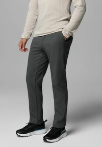 Graue Sporthosen mit tapered Design, ausgestattet mit glattem Stoff und Seitentaschen, kombiniert mit schwarzen Laufsschuhen.