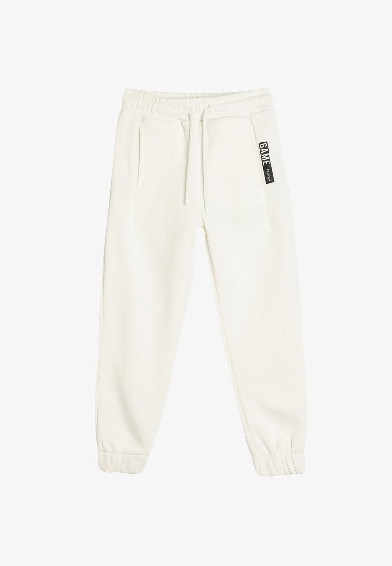 Hvide joggerbukser lavet af blødt materiale, med elastisk talje, sidelommer og et lille sort label foran.