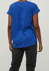 Modrá bavlněná tričko s krátkými zavinutými rukávy, volný střih a zaoblený výstřih, v kombinaci s tmavě šedými džíny.