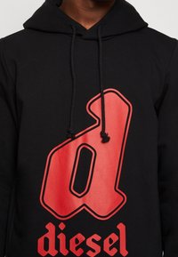 Svart huvtröja med en stor röd "d"-logo och röd text med ordet "diesel", med snoddar vid huvan och en mjuk bomullstextur.