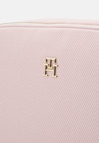 Borsa in tessuto testurizzato rosa con un logo dorato prominente. La borsa ha una chiusura con zip e dettagli di design a righe verticali.