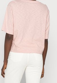 Kortærmet, lyserød t-shirt med en afslappet pasform og en let cropped søm, lavet af blødt, tekstureret stof, parret med hvide kordfløjspants.