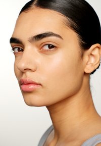 Närbild av ett ansikte med slät hud, naturlig sminkning, fylliga läppar, definierade ögonbryn och rakt svart hår som är bakåtslickat.