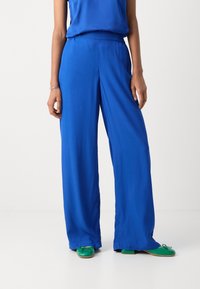 Felblauwe wijde broek met een elastische tailleband, gemaakt van gladde stof. Gecombineerd met groene instapschoenen met een strikdetail.