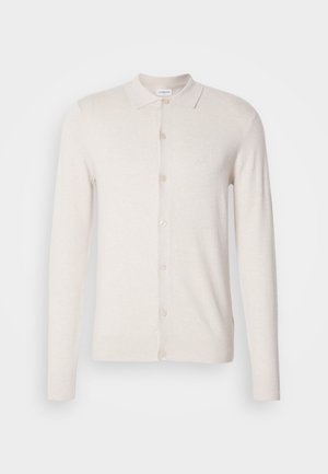 Beiger Cardigan mit langen Ärmeln, Knopfverschluss und einem Kragen. Verfügt über ein dezentes Logo auf der Brust und eine glatte, weiche Textur.