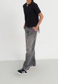 T-shirt nera in cotone con un accento bianco sul collo, abbinata a jeans grigi a gamba larga e sneakers nere con strisce bianche.