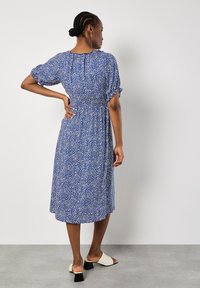 Vestido azul con manchas blancas, mangas cortas abullonadas y cintura ajustada. La longitud llega hasta la mitad de la pantorrilla, fabricado con una tela ligera.