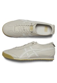 Světle béžové sportovní boty s hladkým koženým svrškem, bílými akcenty, plochými tkaničkami a texturovanou gumovou podešví. Obsahuje logo na stélce.