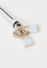 Portachiavi in ecopelle azzurro chiaro con due charm a forma di lucchetto trapuntati e un'etichetta rotonda dorata con il logo 'GUESS'. Include dettagli in metallo dorato.