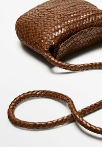 Brązowa torba skórzana o wplecionym wzorze, w kształcie zaokrąglonym, z plecionym paskiem. Tekstura jest gładka, z dokładnym, skomplikowanym wzorem.