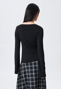 Čierny top s dlhým rukávom a priliehavým strihom, s širokým výstrihom. Kombinovaný s čierno-bielou károvanou sukňou. Jemná textúra.
