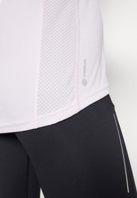 Ljusrosa träningsöverdel med meshdetalj på sidan, kombinerad med svarta leggings som har reflexdetaljer längs sömmarna.