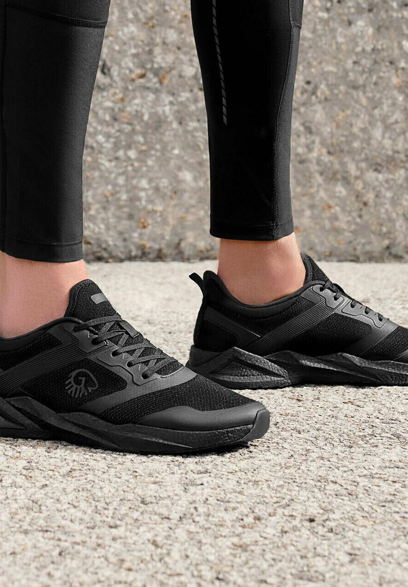 Schwarze Sportschuhe mit einem Obermaterial aus Mesh, strukturiertem Sohlen und Schnürverschluss. Das Design umfasst elegante Linien und minimale Markenakzente.