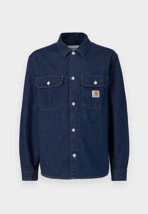 Chemise en denim bleu foncé, avec des manches longues, un devant à boutons, deux poches poitrine et une petite étiquette de marque sur la poche gauche.