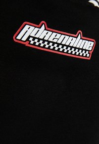 Zwarte T-shirt met een opvallend rood en wit "Adrenaline" logo, met daaronder een geblokt patroon, gemaakt van zachte, gestructureerde stof.