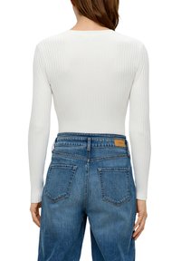 Un haut à manches longues blanc à côtes associé à un jean en denim bleu clair. Le jean présente un design classique à cinq poches et une étiquette de marque en cuir marron.