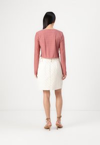 Κόκκινη καρό μακρυμάνικη κοντομάνικη μπλούζα συνδυασμένη με μια λευκή ραφιναρισμένη μεσαίου ύψους φούστα, με διαγώνια ραφή και εφαρμοστή σιλουέτα.