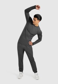 Dunkelgraues Sportset bestehend aus einem Langarmshirt und Jogginghosen, mit einer glatten, feuchtigkeitsableitenden Textur. Weiße Sneakers runden das Outfit ab.