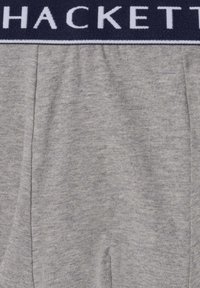 Szare spodnie z tkaniny z elastycznym pasem w pasie, wyposażone w czarny pas z białym napisem "HACKETT".