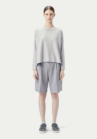 Ljusgrå långärmad topp med avslappnad passform, tillsammans med ljusgrå knälånga shorts. Grå sneakers fulländar outfiten.