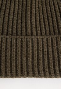 Gros plan sur un tissu tricoté épais et nervuré en olive foncé, montrant des lignes texturées verticales et horizontales sur un matériau doux.