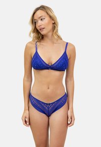 Ensemble de lingerie en dentelle bleue comprenant un bralette triangulaire avec des bretelles ajustables et un bas de bikini taille basse assorti, tous deux arborant des motifs géométriques.