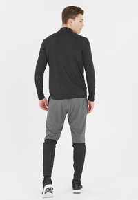 Sort langærmet skjorte med en tætsiddende pasform, parret med grå tapered bukser i en tekstureret stof. Casual sportssko.