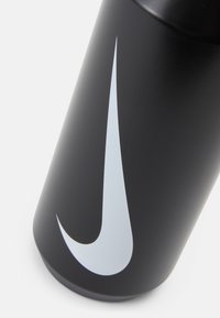 Fekete vízpalack matt felülettel, nagy fehér Nike swoosh logóval. Hengeres forma, sima textúrával.