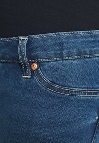 Jeans de ganga azul escuro com um rebite de cobre, um design clássico de cinco bolsos, com costura amarela em contraste e uma textura suave.
