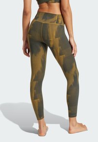 High-waisted leggings in dark green with yellow tie-dye pattern, textured fabric, and contrasting yellow stitching, shown from the back.