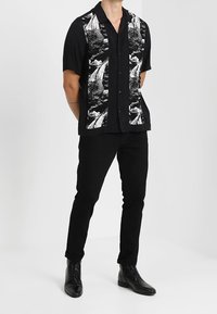 Korte mouwen zwarte shirt met witte natuurprint op de voorkant. Gemaakt in combinatie met zwarte slim-fit broek en zwarte nette schoenen. Gladde textuur, reguliere pasvorm.