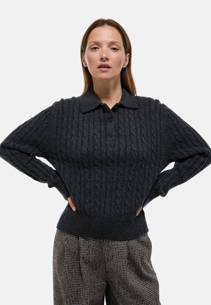 Pull en tricot gris foncé avec un col, des boutons et des poignets côtelés, associé à un pantalon à motif pied-de-poule.
