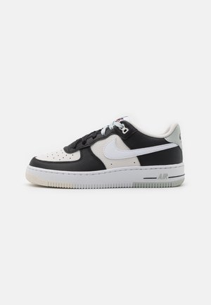 Sneaker basse Nike Air Force 1 en cuir noir et blanc avec un swoosh Nike blanc et une semelle blanche.