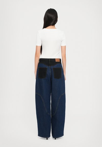 Valge lühikeste varrukatega särk koos laia säärega sinise teksapütsi, millel on vastandlikud mustad tagataskud ja tan nahklabel vööl.