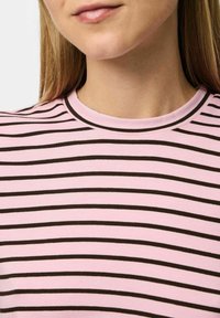 Rozā un brūnā svītrota T-kreklu ar apaļu izgriezumu, mīksts kokvilnas audums un šauras horizontālas svītras. Nav nozīmīgu rotājumu.