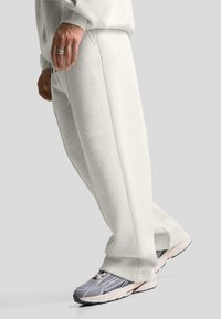 Light grey sweatpants with a relaxed fit, featuring subtle texture and pockets, paired with grey and white athletic shoes.