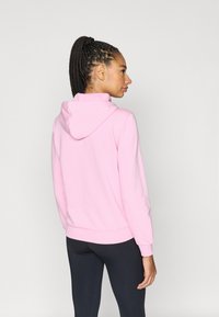 Light pink hoodie with a drawstring hood, ribbed cuffs, and hem. The back is smooth with a relaxed fit, worn over black leggings.