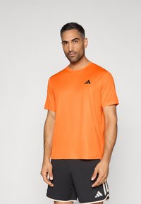 Camiseta deportiva de color naranja brillante hecha de tela ligera, con cuello redondo y un pequeño logotipo negro en el pecho.