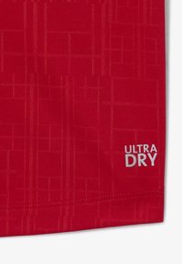 Punainen urheiluvaatekangas, jossa on tekstuuritartunta, ja jossa lukee "ULTRA DRY" valkoisella. Suunnittelu on hengittävä ja kosteuslähtevä.